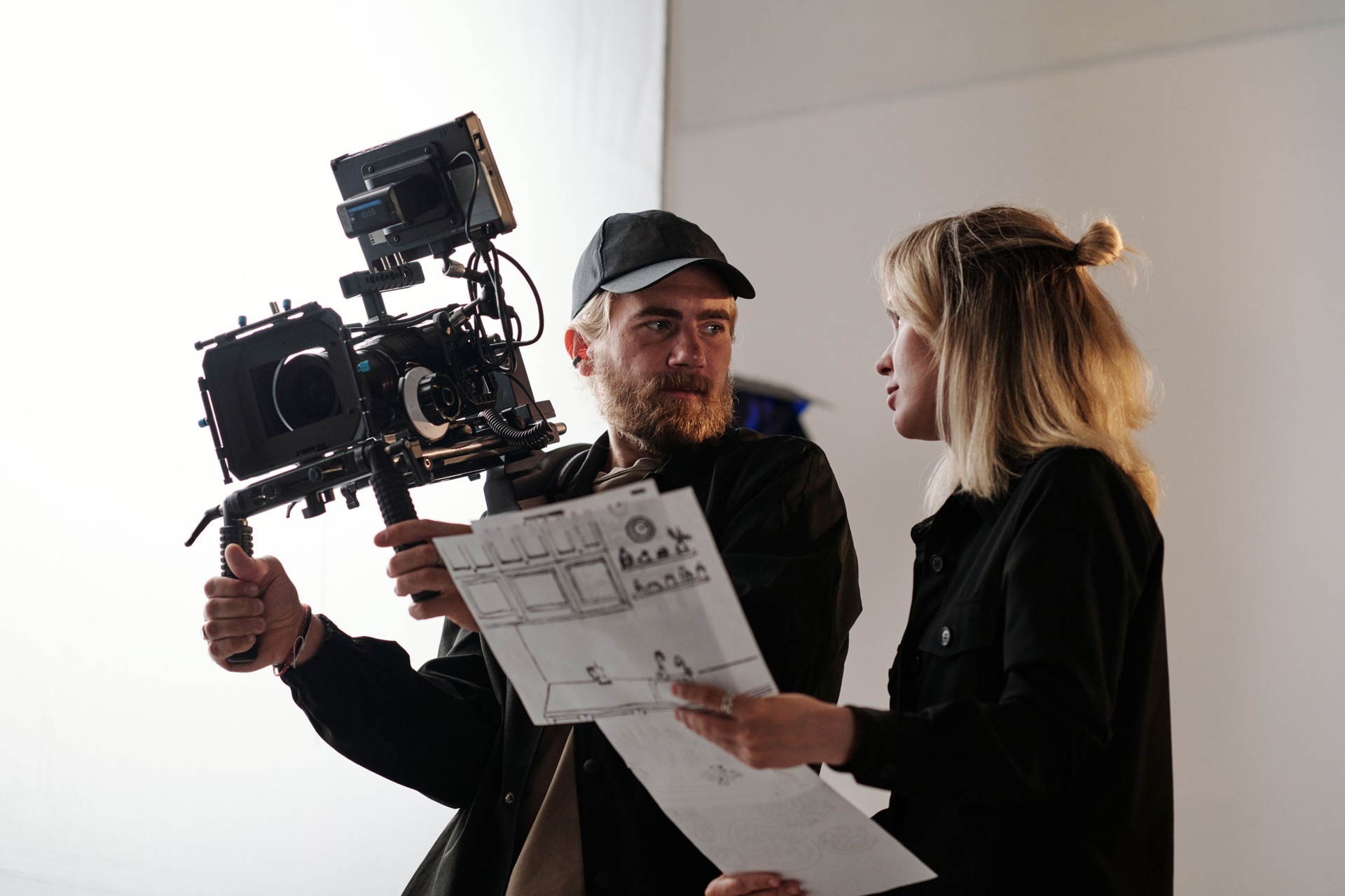 Young bearded cameraman and his assistant consulting about shooting